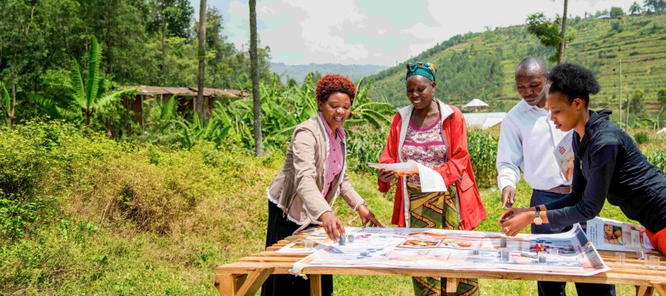 Vier Teilnehmerinnen und Teilnehmer eines Projekts der Deutschen Sparkassenstiftung beschäftigen sich mit dem Thema Klimawandel. Sie stehen um einen Tisch mit Unterlagen im Freien vor einer afrikanischen Landschaft